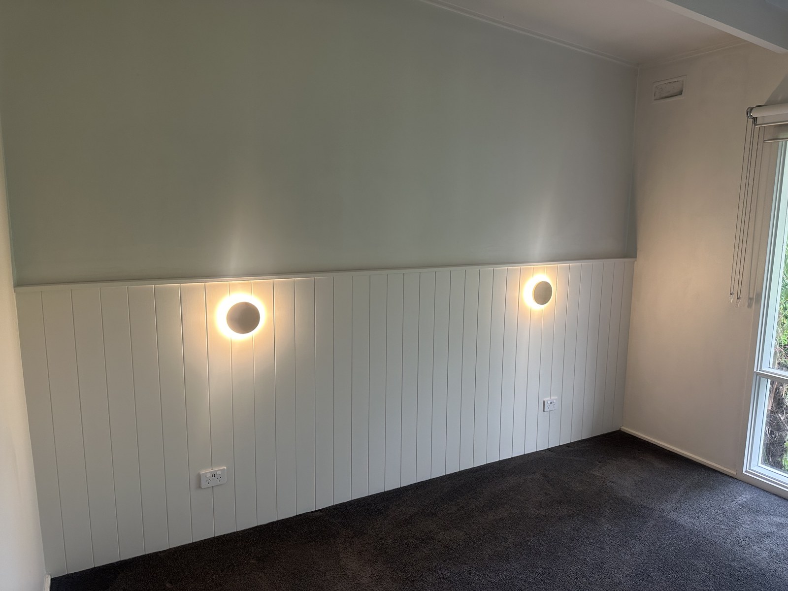 Circular bedroom wall lights above white panelling