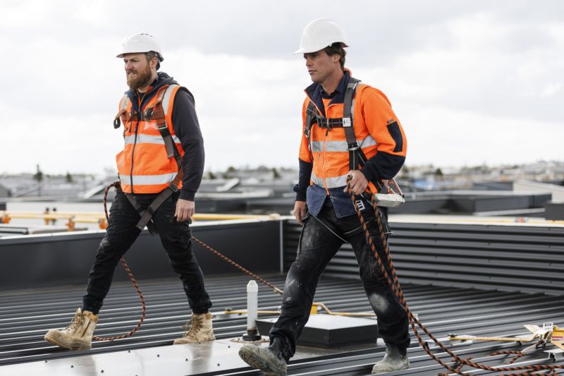 Two workers on a roof wearing hard hats, high-visibility clothing and harness equipment